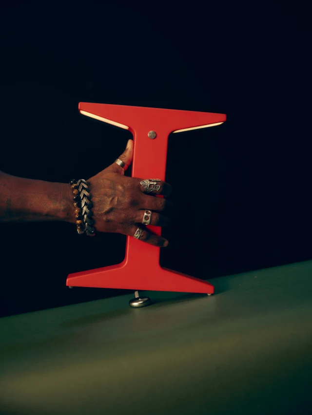 A hand holding a red Gantri wireless lamp above its charging base